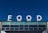 Large white letters spelling 'FOOD' are prominently displayed atop a building against a clear blue sky. The building facade features multiple rectangular windows with a modern design.