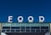 Large white letters spelling 'FOOD' are prominently displayed atop a building against a clear blue sky. The building facade features multiple rectangular windows with a modern design.
