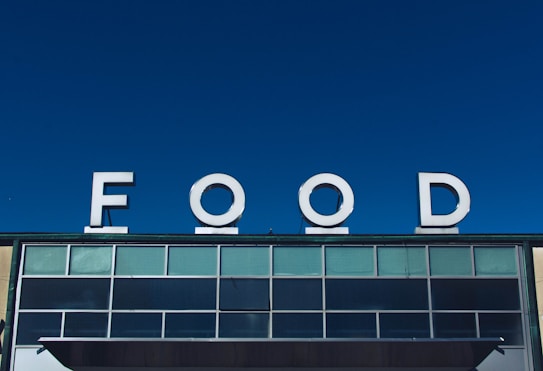 Large white letters spelling 'FOOD' are prominently displayed atop a building against a clear blue sky. The building facade features multiple rectangular windows with a modern design.