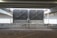 Large metallic cooling units are positioned under a steel-beamed structure in an industrial setting. The units have a grid design on their fronts and are elevated on a concrete platform marked with numbers 347 and 348. The scene is partially lit by natural light filtering through the wide windows behind them, and there are visible signs of rust on the beams.