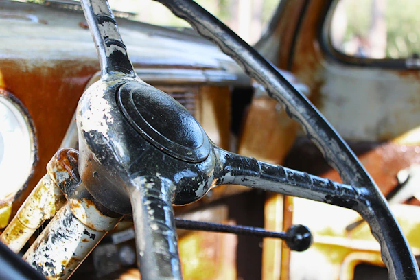 Close-up of a weathered hand gripping a steering wheel inside a vintage Bronco, sunlight streaming through the windshield.