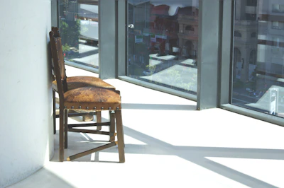 A minimalist wooden chair with soft cushions placed beside a window with natural light