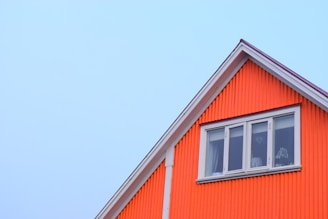 A vibrant house roof showcasing a blend of warm red and orange hues under a clear blue sky.