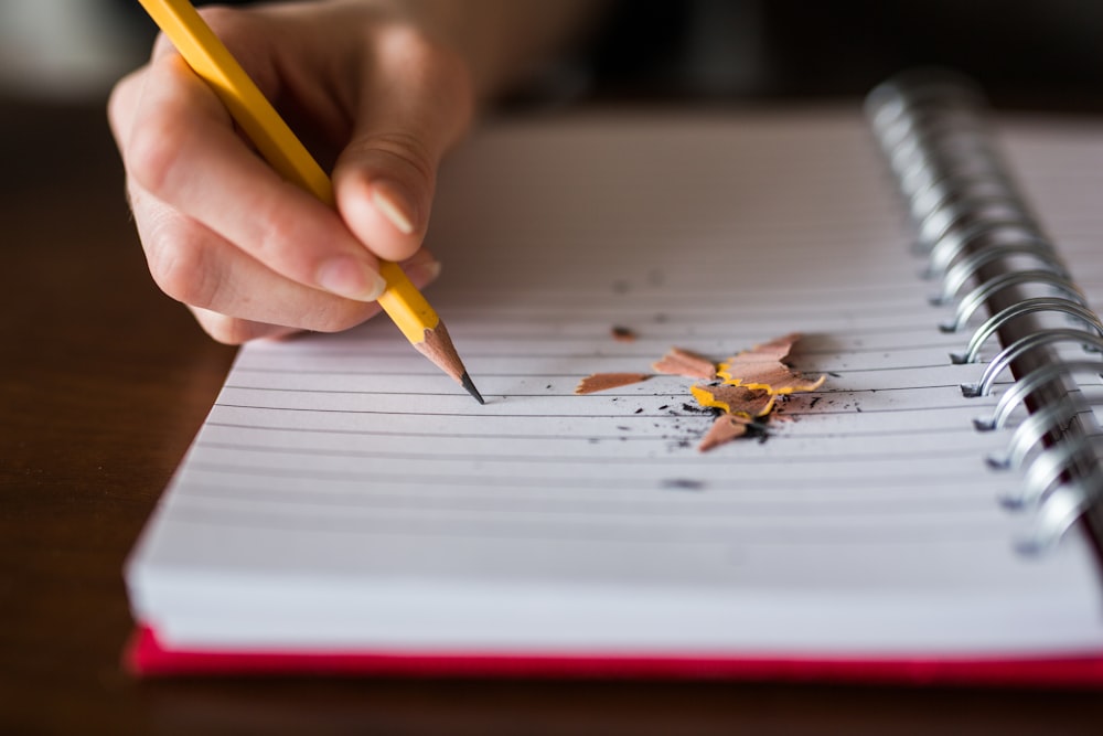 pessoa segurando lápis escrevendo no caderno