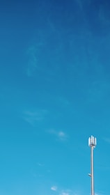 A tall cellular tower stands against a vast blue sky with slight cloud formations.