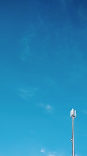 A tall cellular tower stands against a vast blue sky with slight cloud formations.