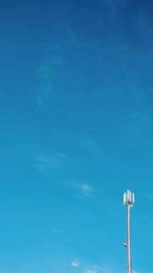 An engineer inspecting a cell tower against a clear blue sky.