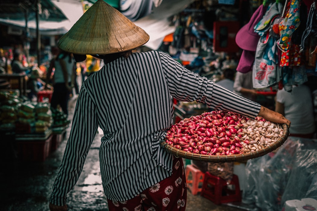 woman carrying a basket of vegetables through a busy market