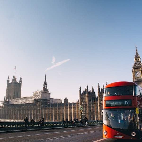 red double-decker bus passing Palace of Westminster, London during daytime