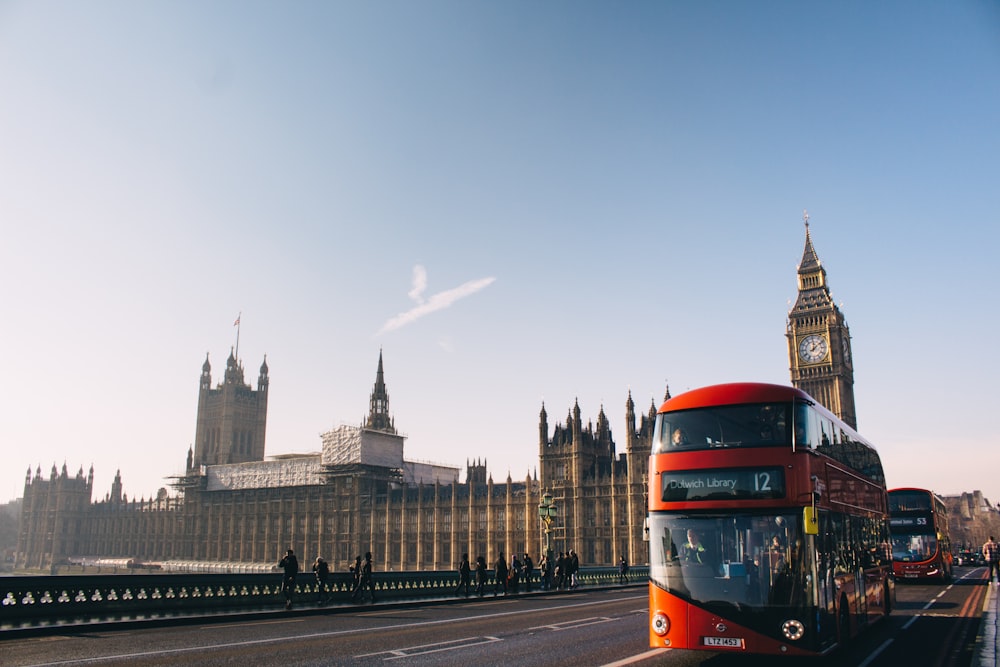 roter Doppeldeckerbus, der tagsüber am Palace of Westminster, London, vorbeifährt