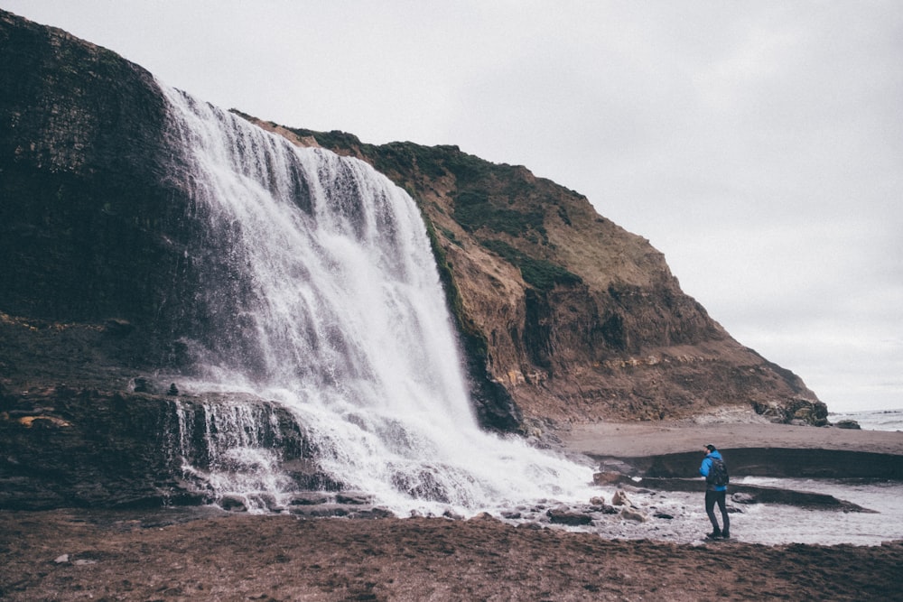 photo of man standing near waterfalls