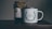 A rustic setting features a jar of organic certified honey with a handmade paper cover next to a white enamel mug. The mug is adorned with an illustration of green leaves encircling the words 'Head Gardener.' These items are placed on a wooden surface, suggesting a cozy, natural atmosphere.