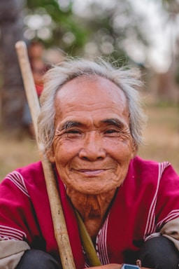 portrait photography,how to photograph if you are lucky, you grow old and become a village elder. for the karen people, they do not keep record of their ages. instead, they recall a certain past event that occurred when they were born.; man holding brown stick smiling