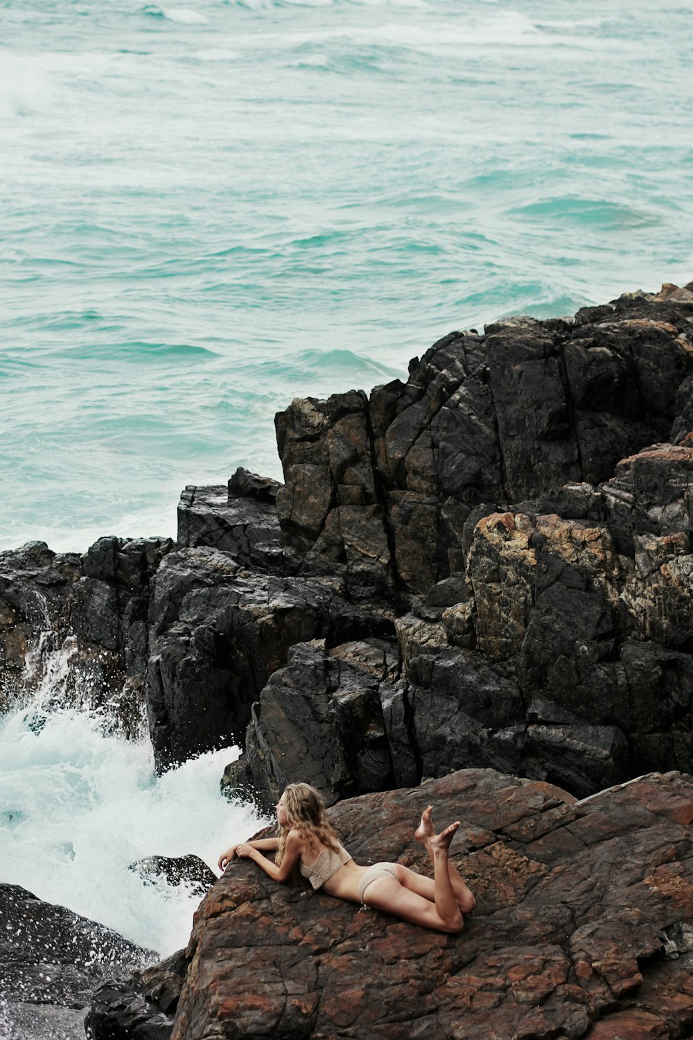 woman lying on rock formation on seashore