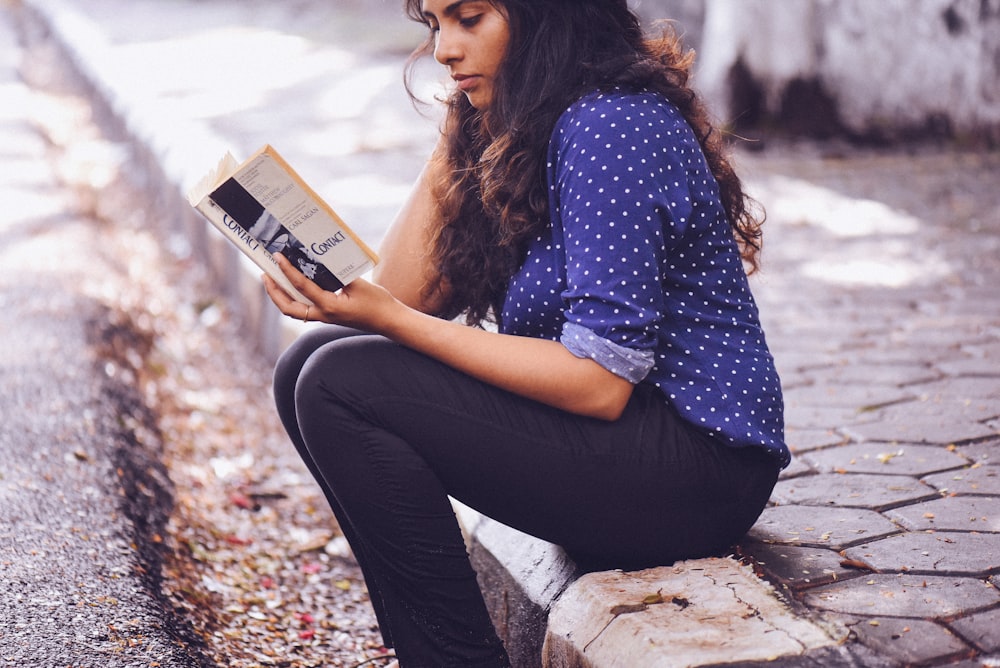 Frau sitzt auf Gosse und liest Buch