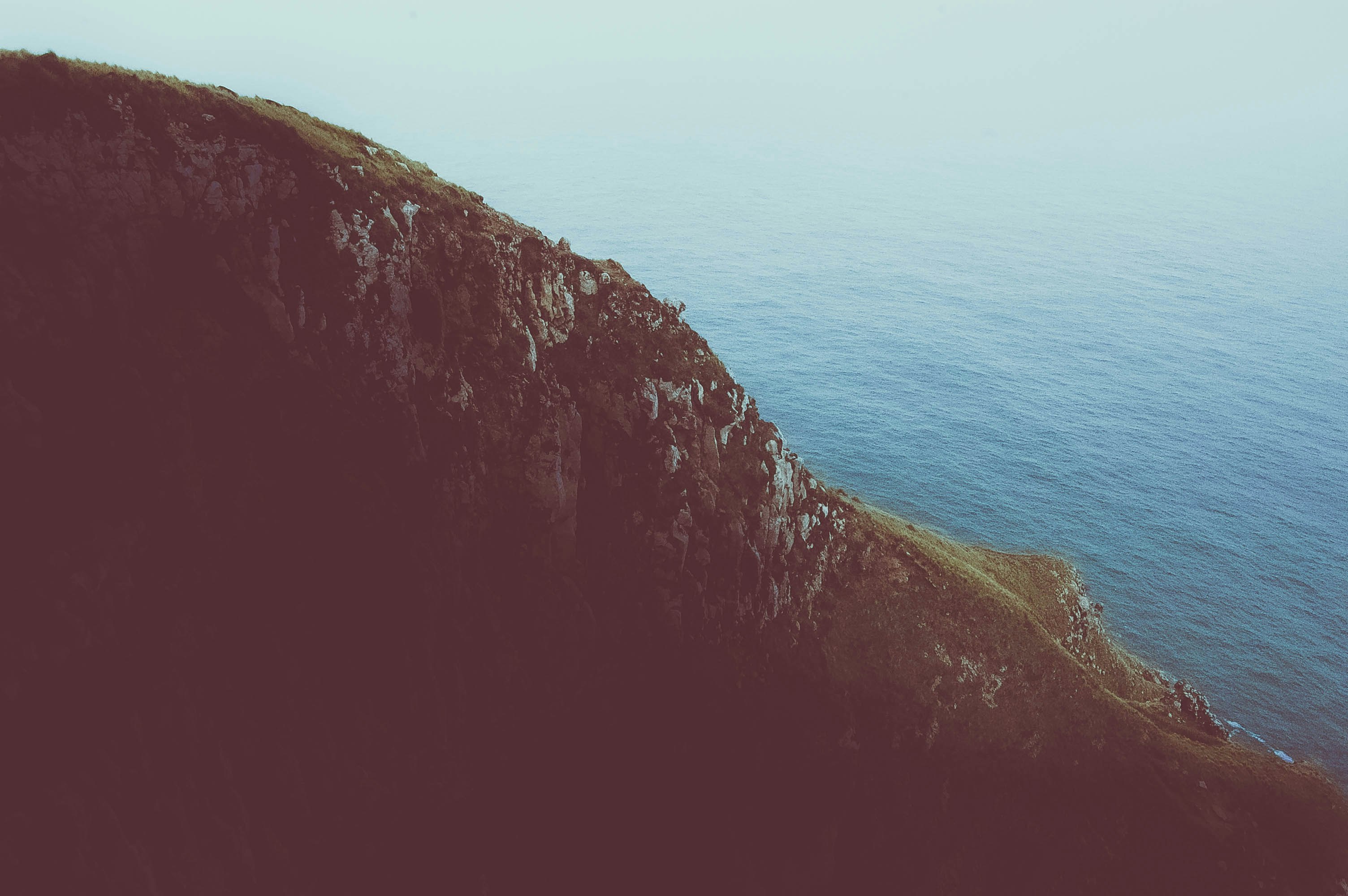 photo of cliff near calm sea during daytime