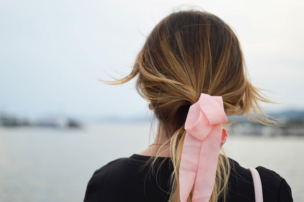 Fotografia di messa a fuoco della donna con l'arco dei capelli rosa rivolto verso lo specchio d'acqua