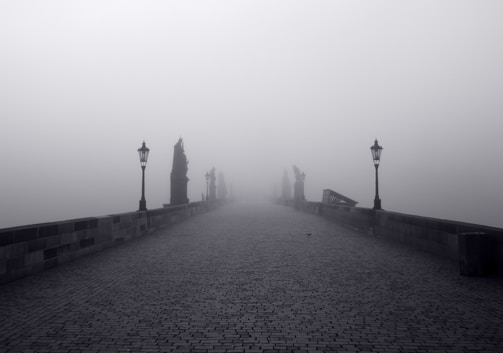 A foggy ancient stone bridge at dusk, surrounded by dense forest.