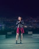 A model wearing a sleek cyberpunk jacket standing against a glowing neon cityscape at night.