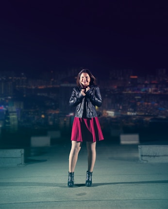 A model wearing a sleek cyberpunk jacket standing against a glowing neon cityscape at night.