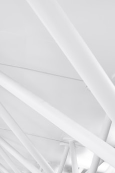 A complex array of white structural beams crisscrossing at various angles, creating a geometric and modern architectural pattern.