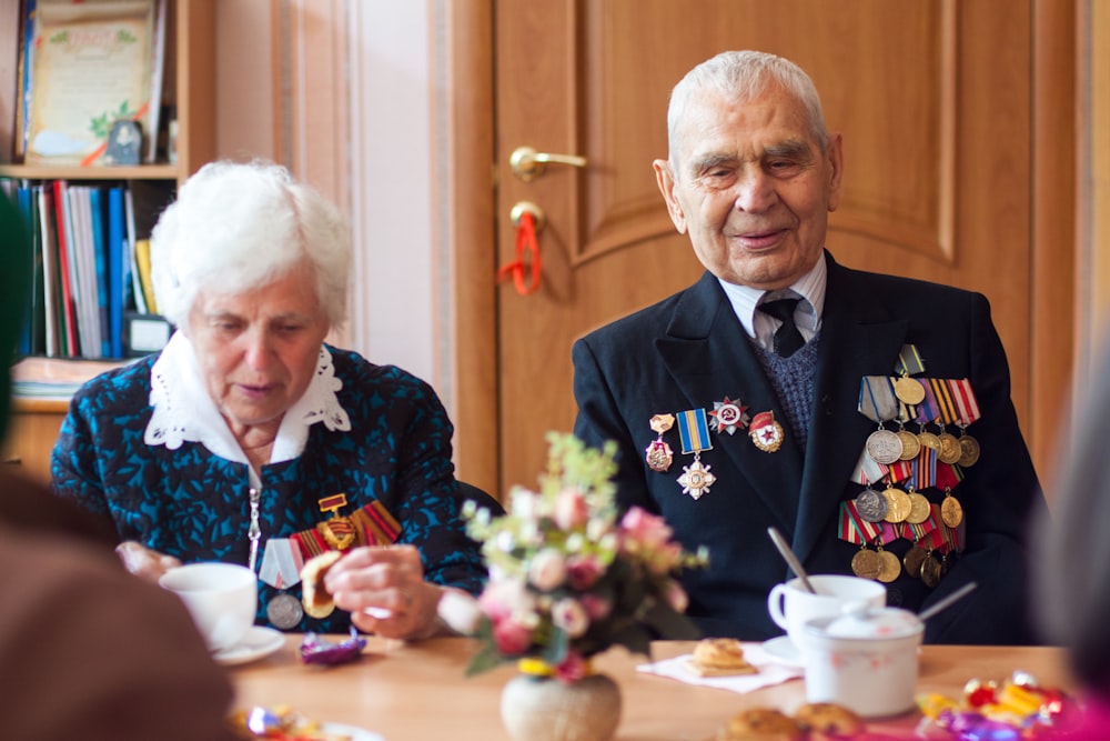 A retired and old Ukraine soldier sitting with his wife and medals on his jacket.