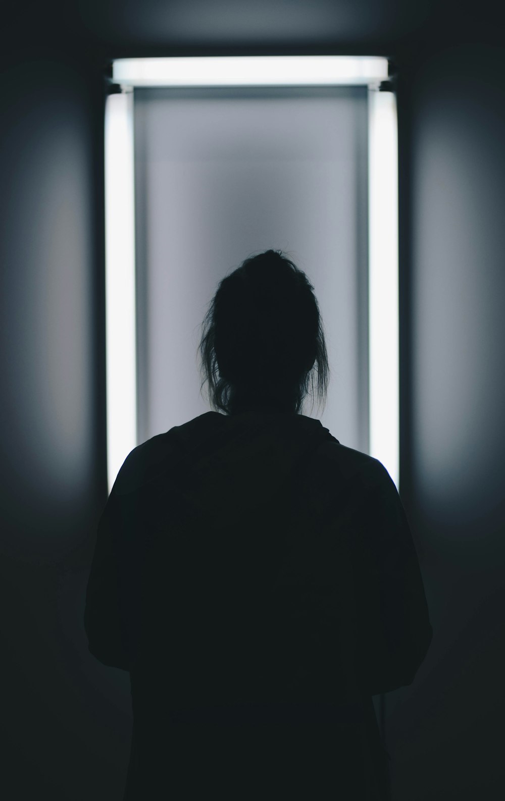 silhouette photo of person standing in front of mirror