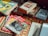 A collection of vintage magazines and books is spread out on a woven mat. The magazines feature topics like cars and motorcycles, with titles such as 'Motorcycle Mechanics' and 'Auto Car'. The books include older editions with classic designs and titles. The lighting gives a nostalgic feel to the scene.
