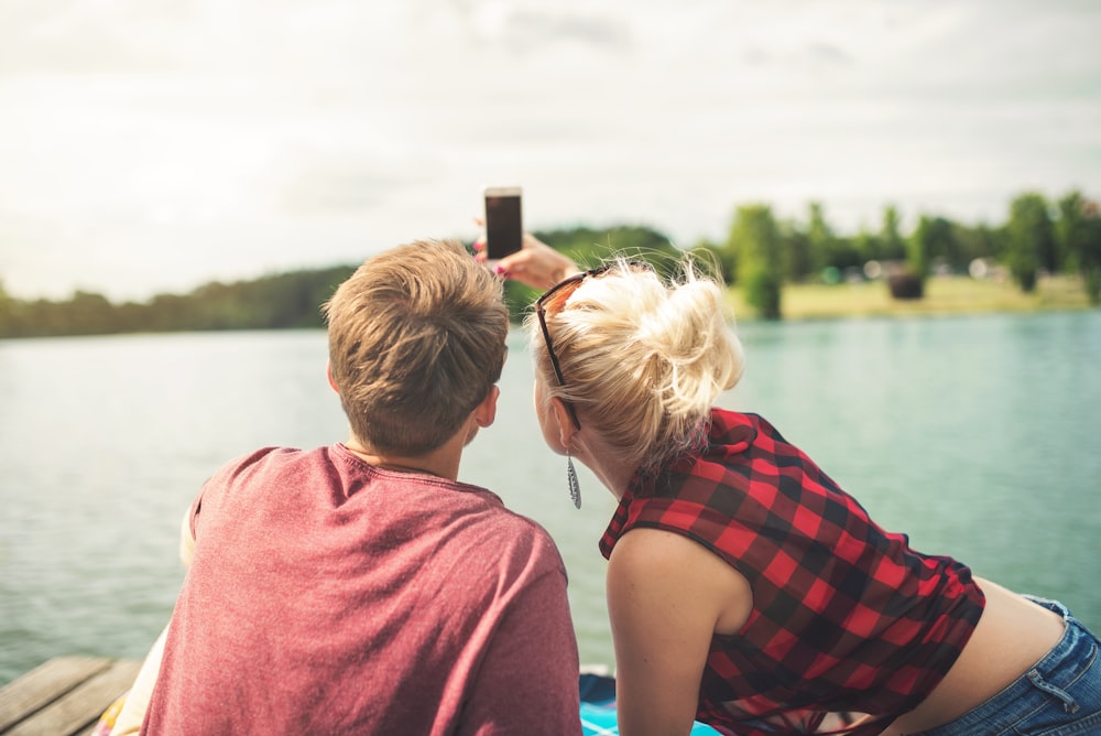 woman and woman sitting on dock both holding one smartphone