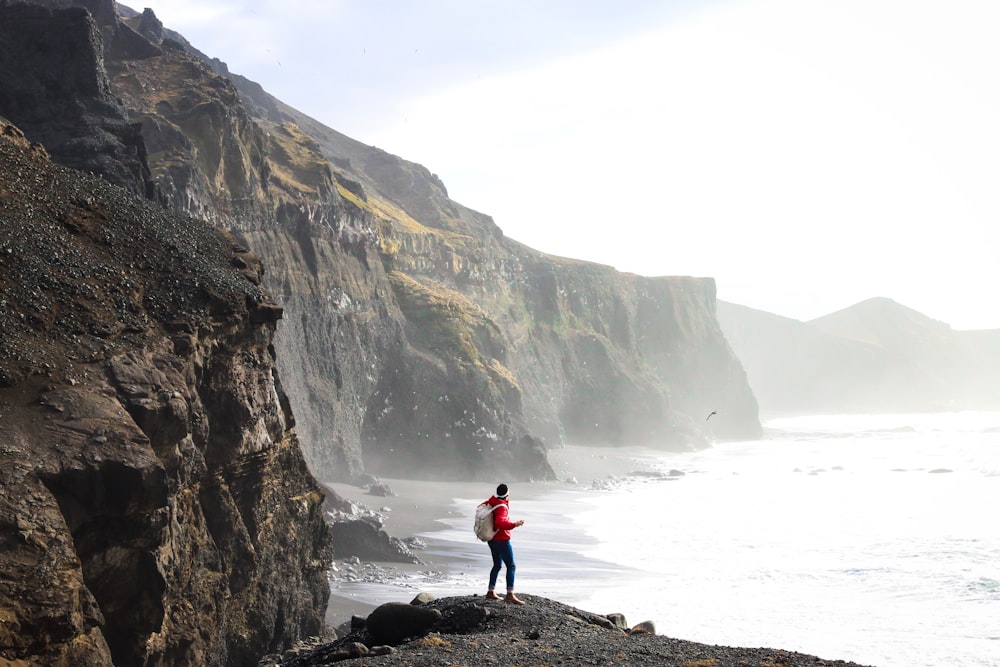 person standing on cliff near body of water during daytime