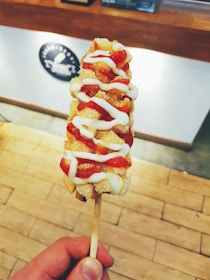 A smiling customer holding a corn dog with melted cheese stretching as they take a bite.