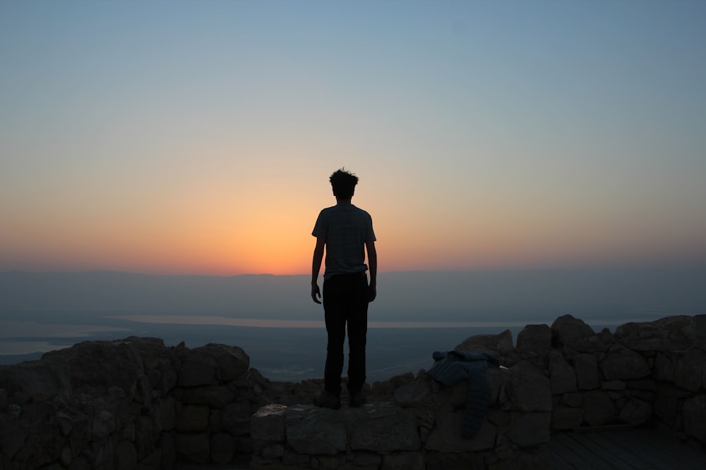 man standing on white stones looking in sea