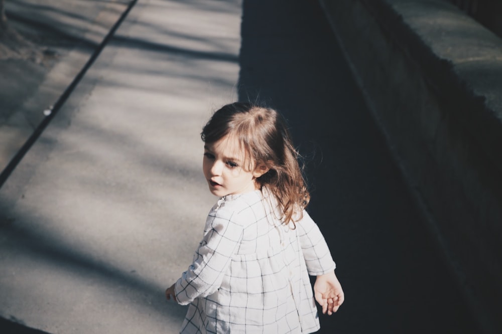 bambina che cammina sulla strada di cemento grigia durante il giorno