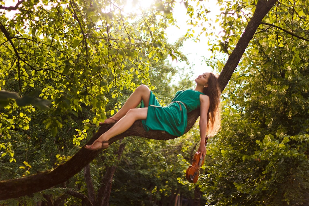 Mujer en vestido verde acostada en la rama de un árbol