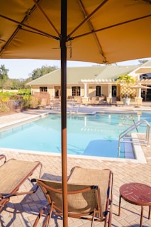 Outdoor pool area at a hotel with orange lounge chairs and guests relaxing under umbrellas