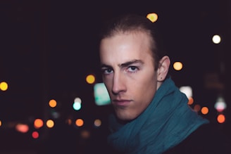 A vibrant teal scarf casually wrapped around a man's neck against a city street backdrop.
