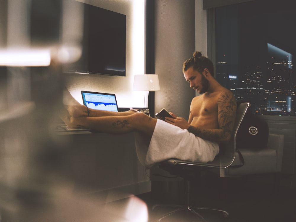 man sitting on rolling chair while using smartphone