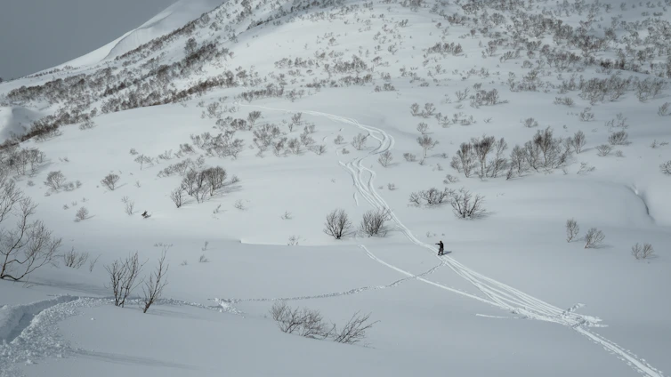 A serene snowy mountain landscape with a lone skier enjoying a peaceful descent under a clear blue sky.