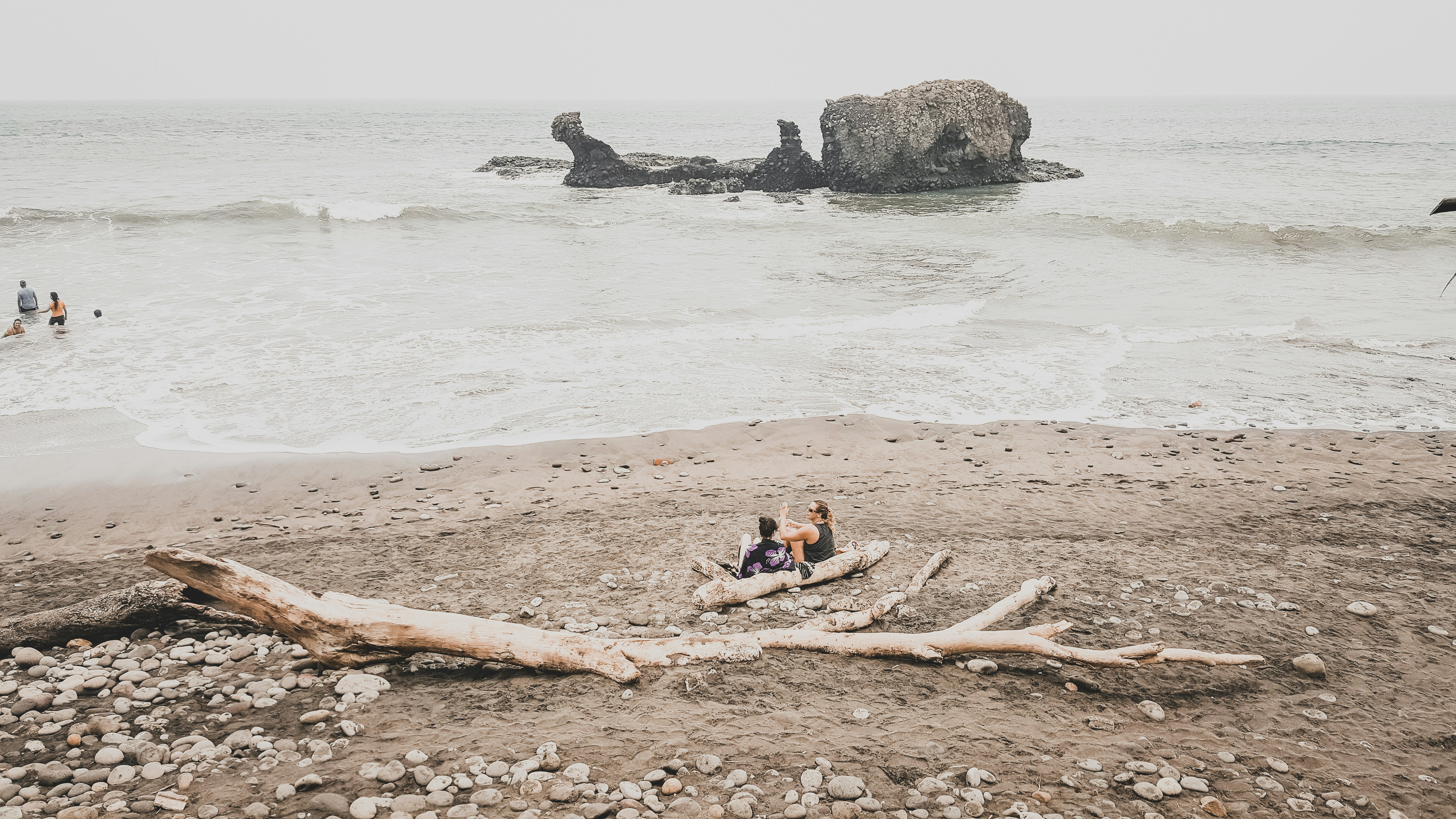 two men's sitting on shore near gray rock formation at daytime