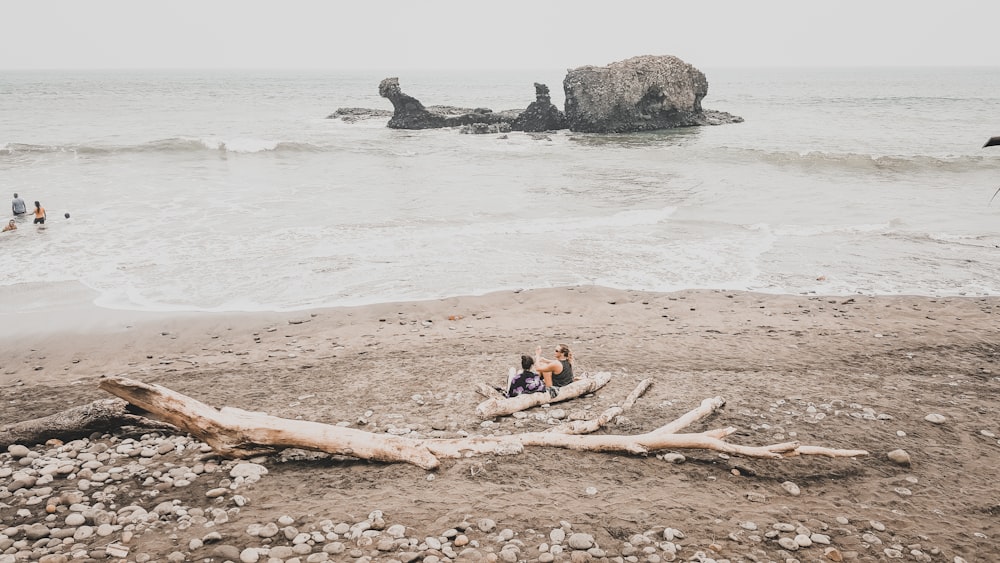 two men's sitting on shore near gray rock formation at daytime