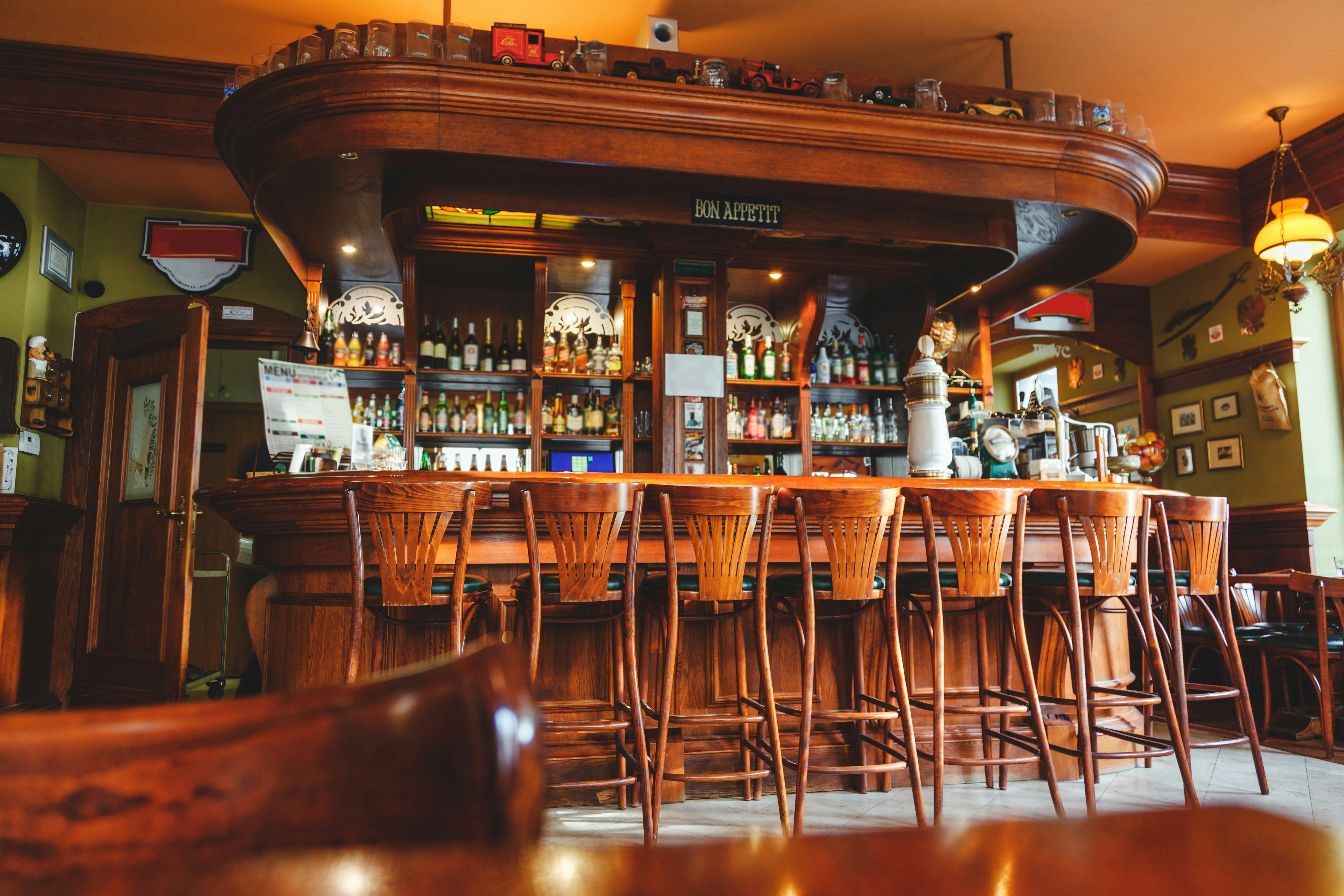 Bar counter with vintage bottles, warm lighting, and wooden stools