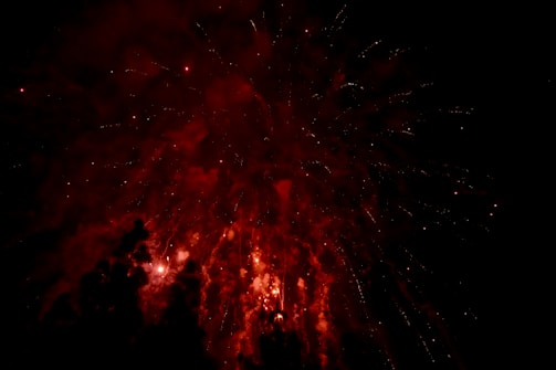 Explosions of vibrant red fireworks illuminate the night sky, creating a mesmerizing display of lights and colors against a dark background.