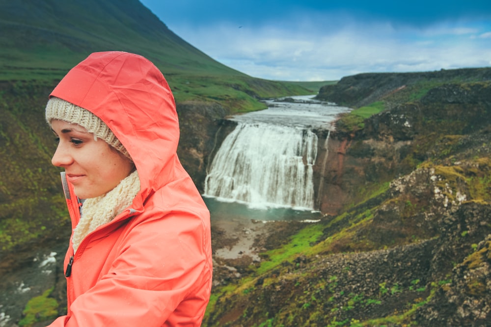 woman wearing pink hoodie standing on top of mountain near waterfalls