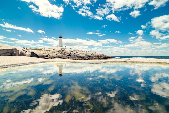 lighthouse tower near calm water under white clouds and blue sky in Peggys Cove Canada