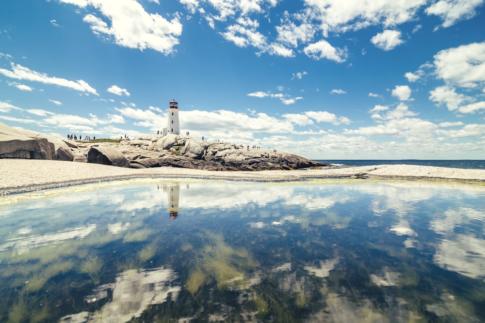 Torre do farol perto de água calma sob nuvens brancas e céu azul