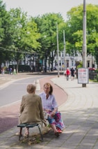 A traveler and a local elder sitting together on a bench, engaged in warm conversation.