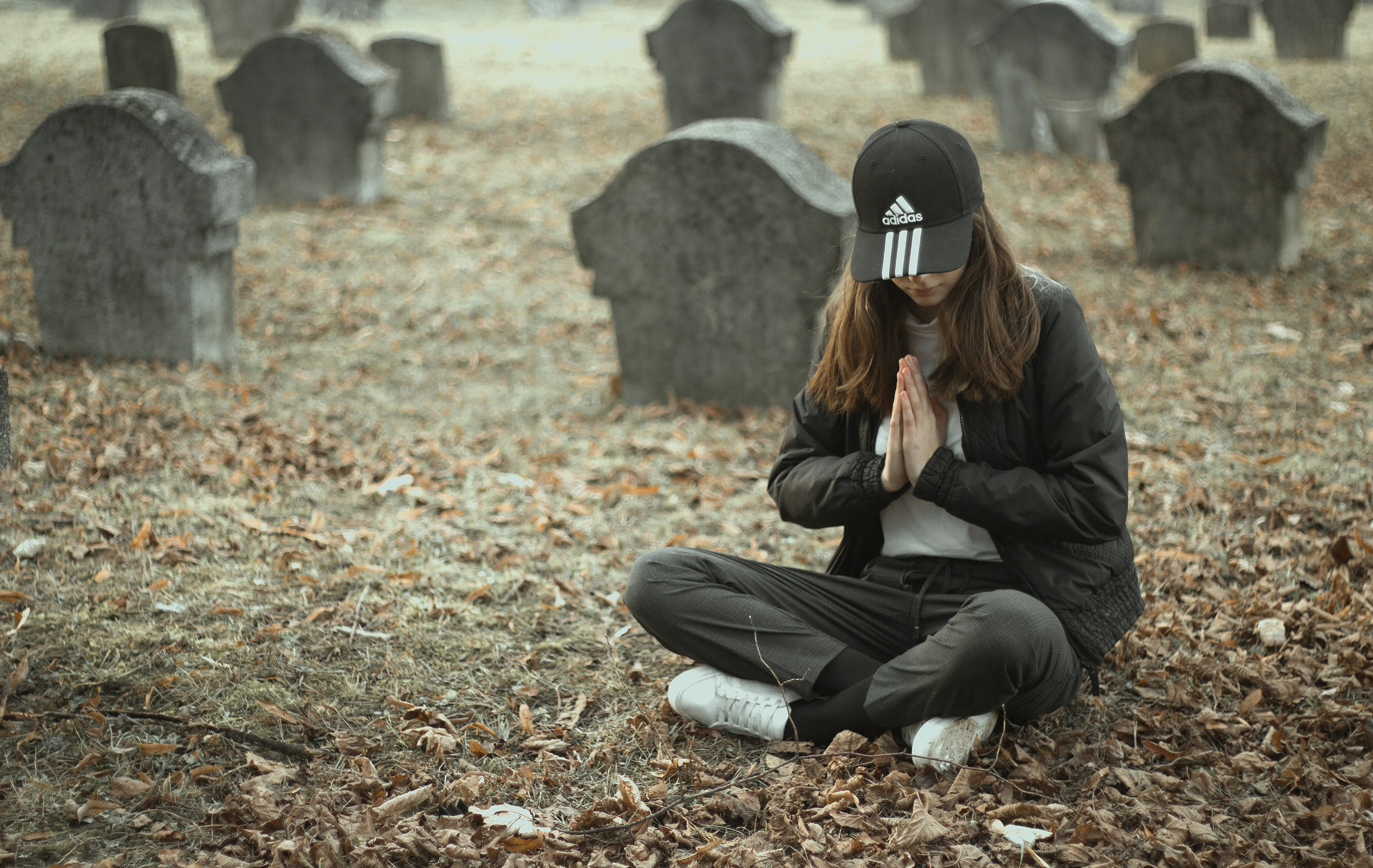 Woman in black jacket and black pants sitting on ground with dried