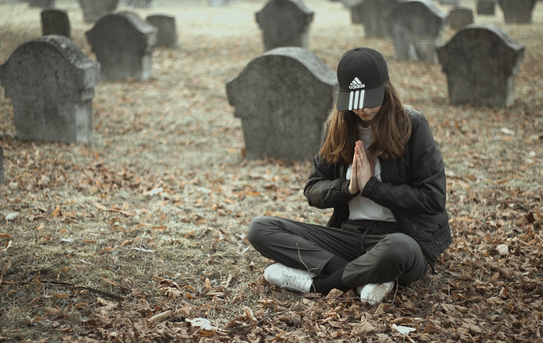 woman in black jacket and black pants sitting on ground with dried leaves