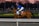 A jockey dressed in blue and yellow riding attire is mounted on a brown racehorse. The horse wears a blue cap and is marked with the number 16. They are on a race track bordered by white railings with a backdrop of a dusky sky and blurred trees.