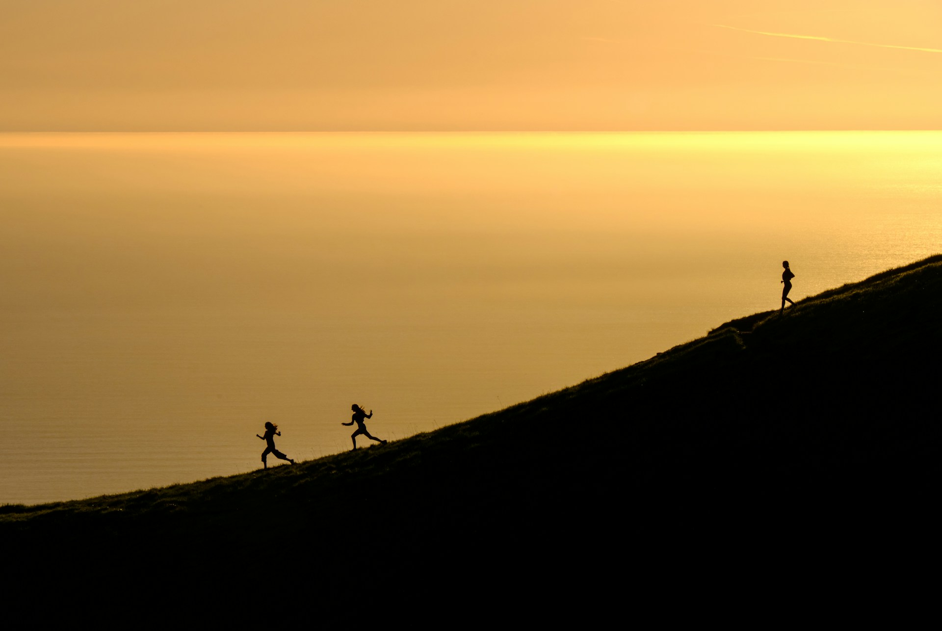 three persons running downhill during golden hour